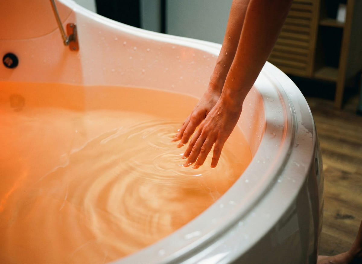 Mains touchant l'eau orange dans une baignoire.